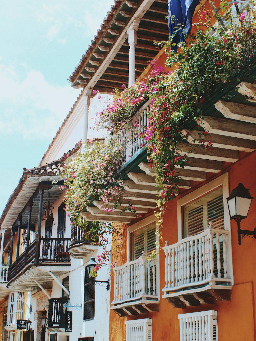 Colorful colonial buildings with flower-covered balconies under a blue sky.