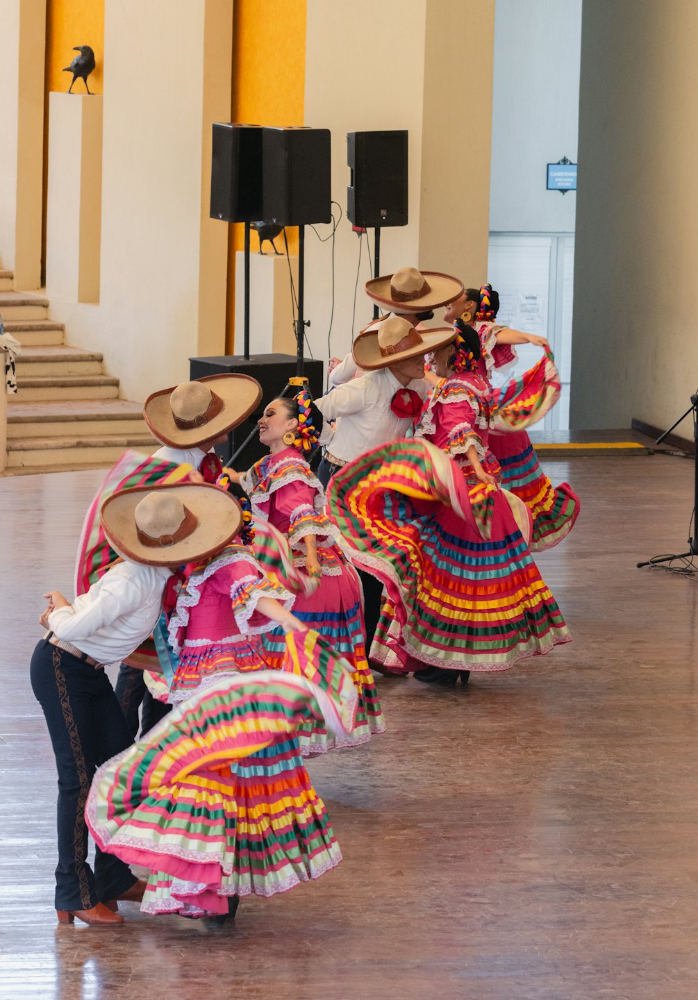 Dancers in colorful folk costumes perform indoors.