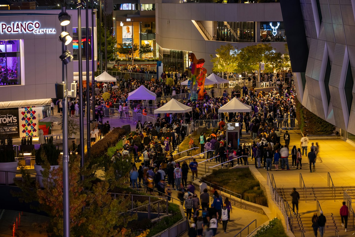People walking through a brightly lit urban plaza at night.